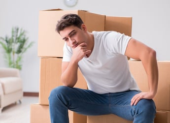 Young man thinking alongside boxes